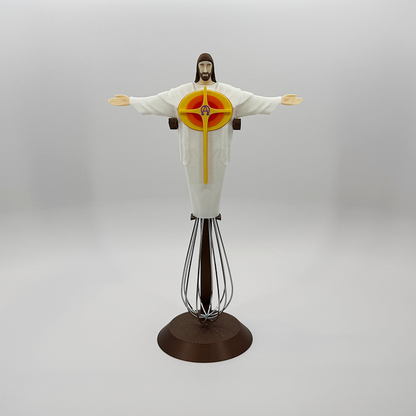Eggbeater Jesus whisk ornament on a bronze display stand, arms outstretched above the wire whisk
